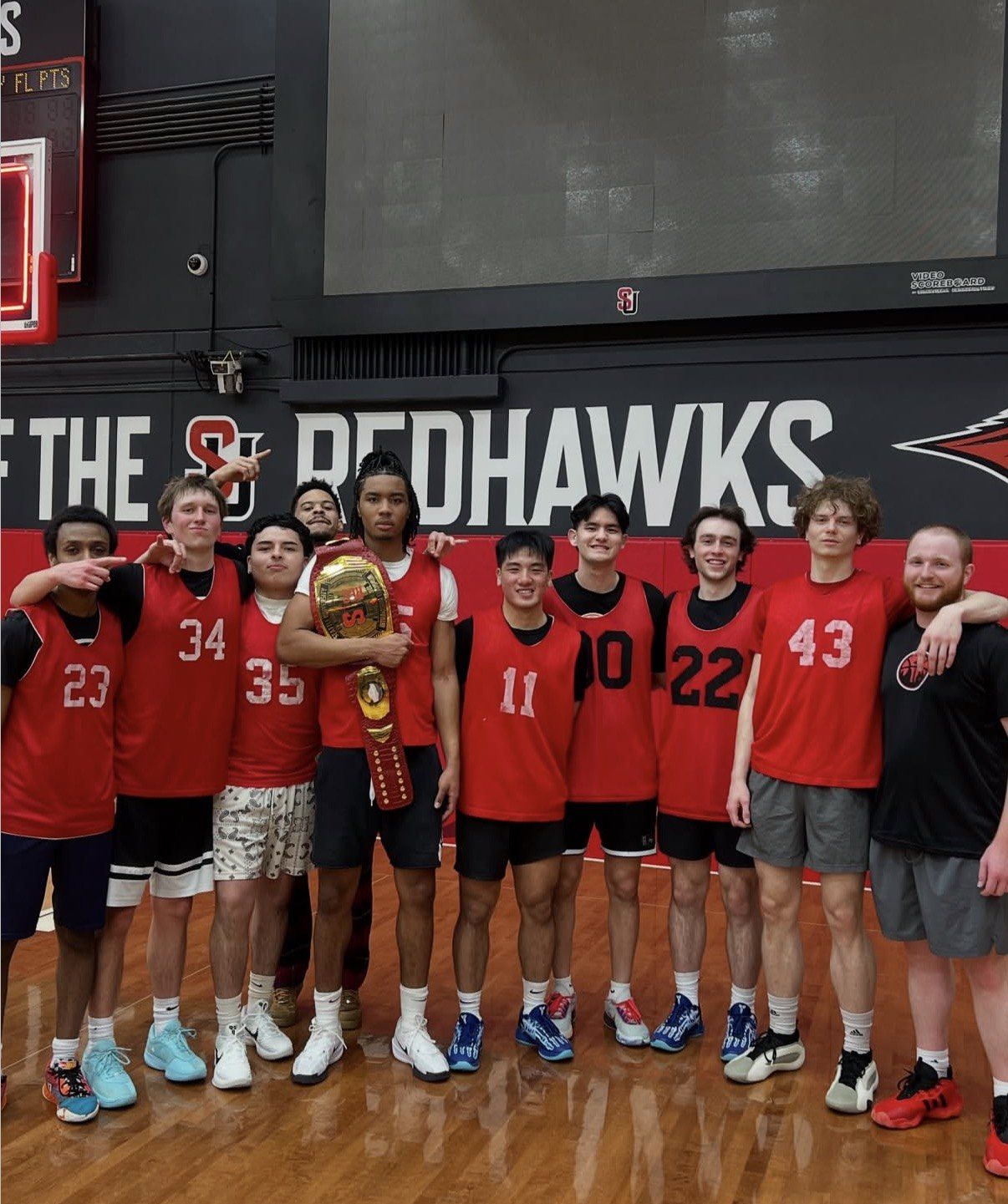A basketball team in red jerseys with a championship belt in the Seattle University gym